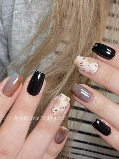 Stylish manicure with black, grey, and nude nail designs, featuring abstract patterns.