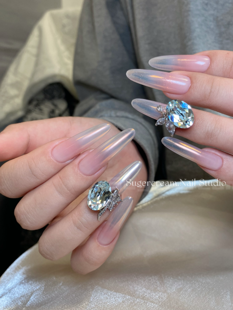 Long, clear nails with large rhinestone accents on two fingers.