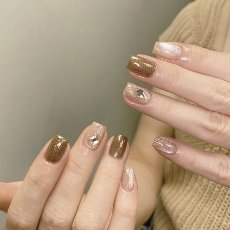 A close-up of hands showing an elegant manicure with brown and nude nails and metallic accents.