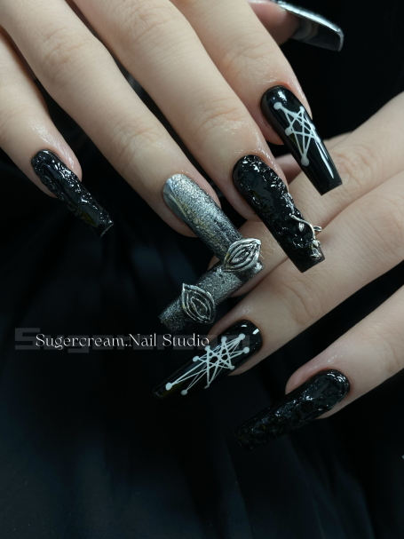 Long black nails with silver accents and intricate designs, featuring a bow and spider motifs.