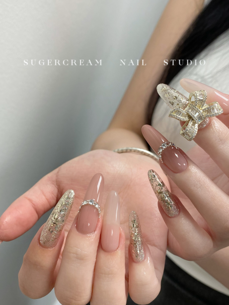 Elegant nails featuring a nude base with gold accents and a decorative ring.