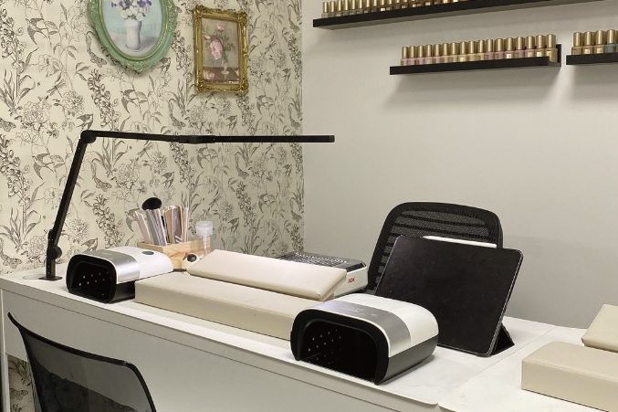 A neatly organized desk with stationery and a modern lamp against a patterned wall.