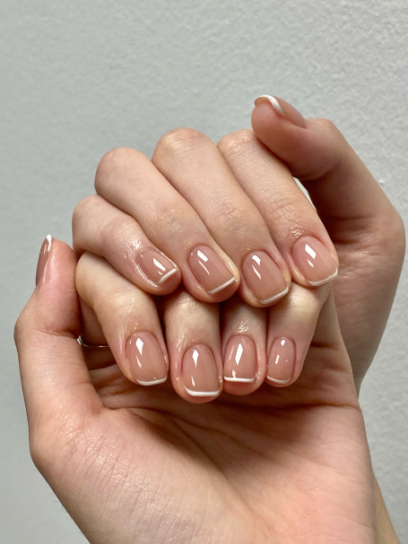 Close-up of hands showing elegant, manicured nude nails with a French tip design.