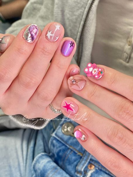 Close-up of hands with various nail designs and colours, including glitter and floral patterns.