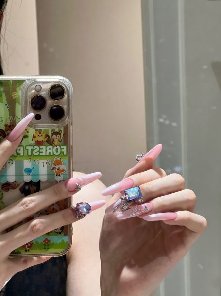 A hand with long pink nails holding a smartphone with a colourful case.