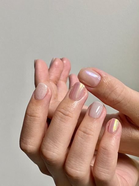 A close-up of hands showcasing nails with a nude and iridescent finish.