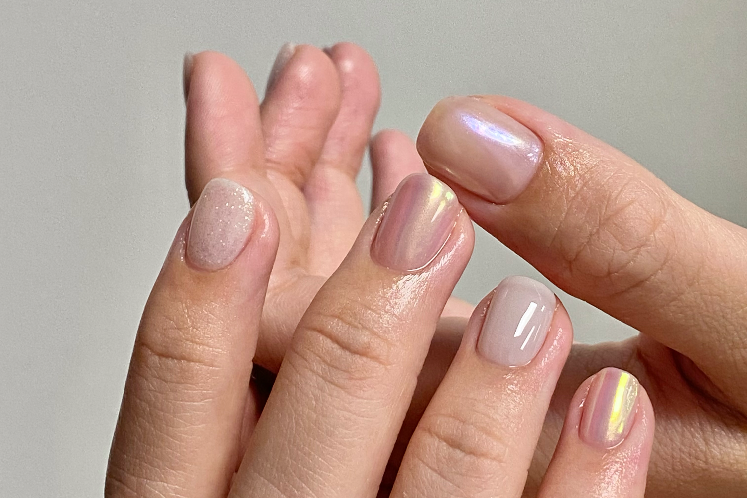 Close-up of hands with manicured nails in soft, neutral shades and iridescent accents.