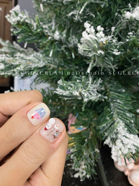Light pink nails with festive designs next to a frosted Christmas tree.