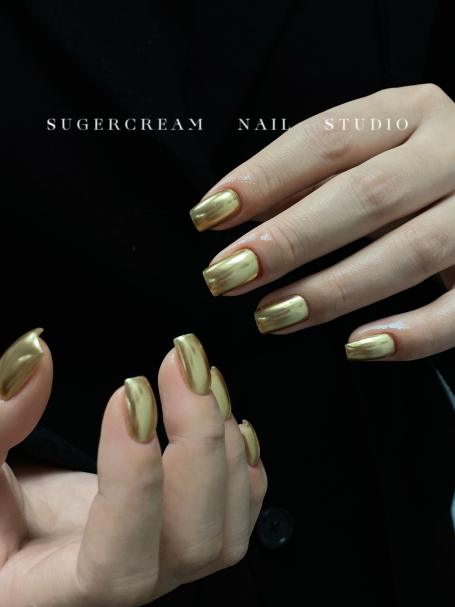 Hands with glossy gold nail polish on display against a dark background.