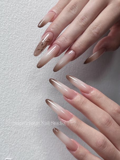 Long, almond-shaped nails with a gradient from nude to brown tips.