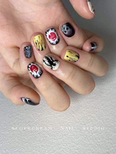 A hand displaying colourful, artistic nail designs with various patterns and motifs.