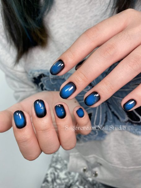 Hands with blue ombre nails, featuring a glossy finish and black tips.