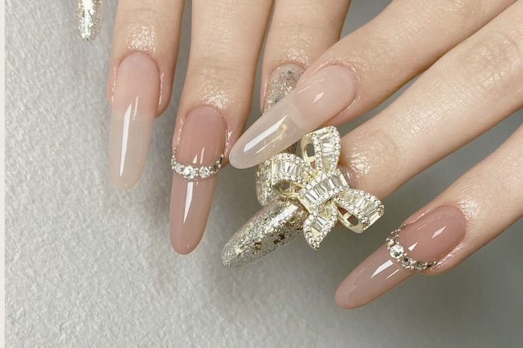 Elegant long nails in nude and clear shades, adorned with sparkly rings and gems.
