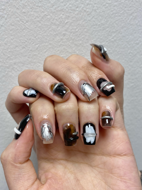 A hand displaying stylish black, silver, and brown nail art designs.