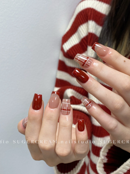 Close-up of manicured nails with red and nude designs, featuring stripes and patterns.